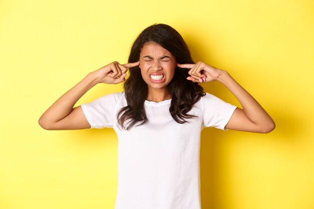 Portrait of annoyed and pissedoff africanamerican girl shut her ears and grimacing from loud awful