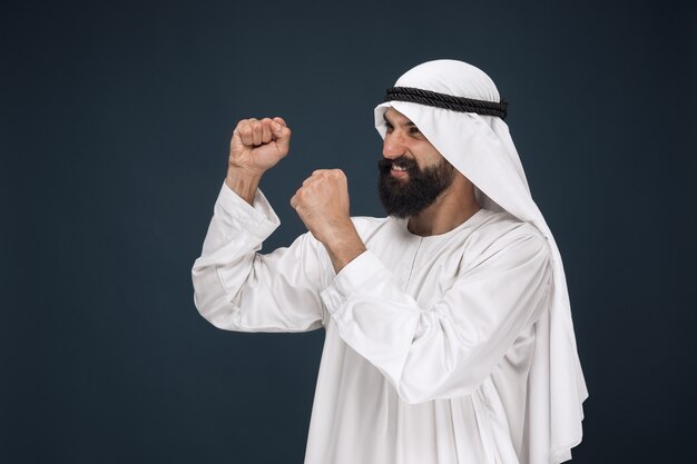 紺色の空間にアラビアのサウジアラビアの実業家の肖像画。立って、笑顔で祝う若い男性モデル