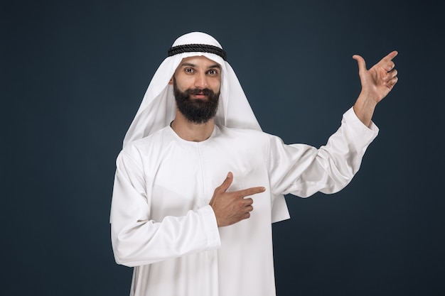 Free photo portrait of arabian saudi man. young male model smiling and pointing.