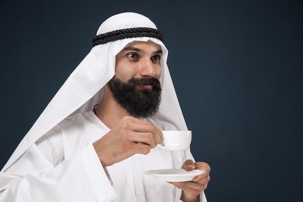 portrait of arabian saudi man. Young male model standing and drinking coffee or tea.