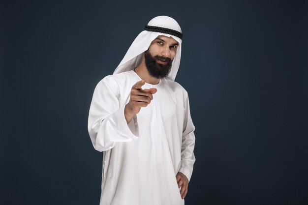 portrait of arabian saudi sheikh. Young male model smiling and pointing or choosing.
