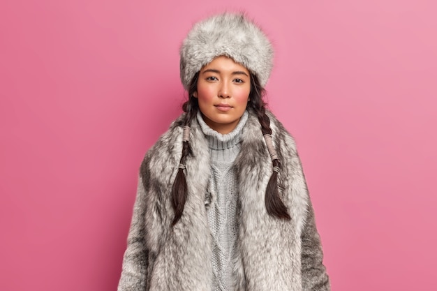 寒い気候のための2つのピグテールドレスと北極のwoamanの肖像画はピンクの壁に隔離された灰色の毛皮のコートと帽子を着ています
