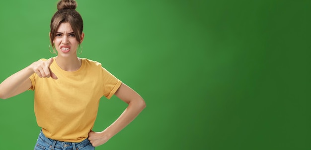 Free photo portrait of arrogant impolite young woman in yellow tshirt pointing at camera squinting and