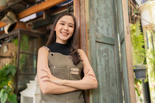 Portrait of asian adult female woman wear apron standing at entrance of her workshop pottery studio incasual cloth relax smiling confident and warm welcomeasian woman with her home studio workshop