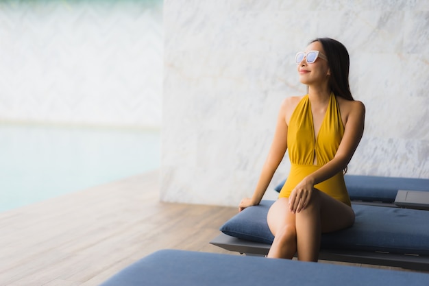 Foto gratuita il sorriso felice della bella giovane donna asiatica del ritratto si rilassa intorno alla piscina all'aperto nella vacanza di festa