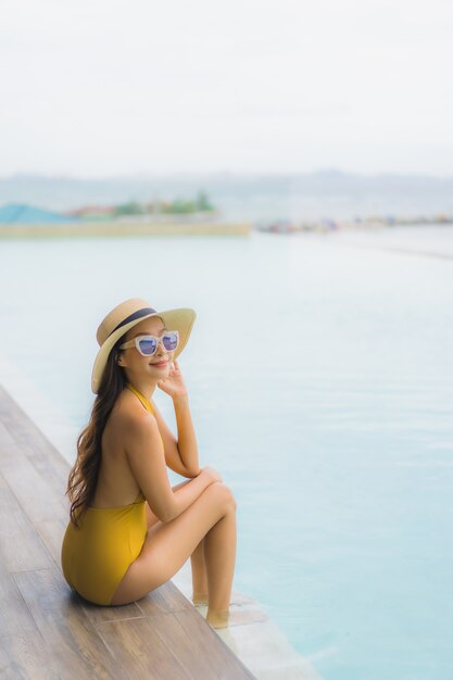 Улыбка азиатской красивой молодой женщины портрета счастливая ослабляет вокруг открытого бассейна в каникулах праздника