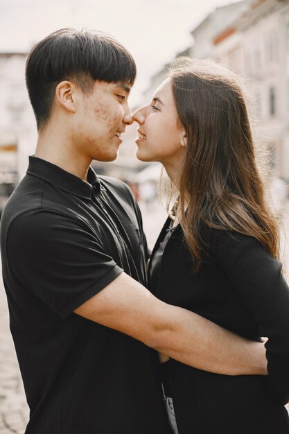 Portrait of an asian boy and his caucasian girlfriend in casual wear standing on  street. Couple is going to kiss each other while walking together in city