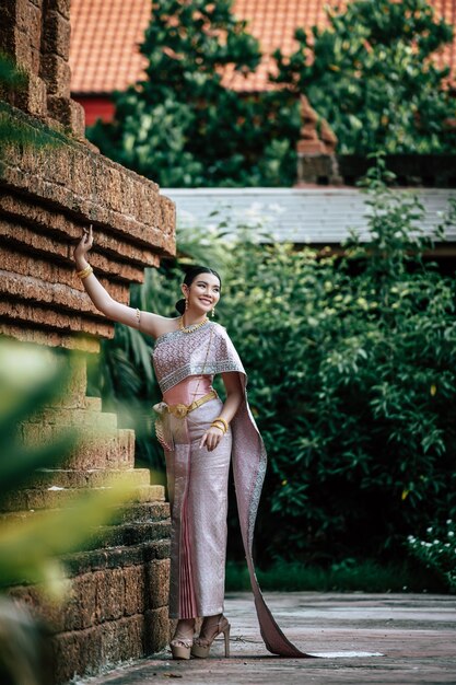 Free photo portrait asian charming woman wearing beautiful typical thai dress identity culture of thailand in ancient temple or famous place with gracefully pose