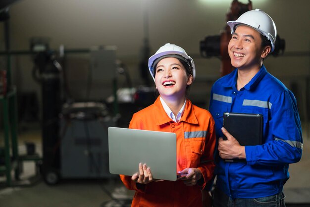 Portrait of asian emgineer male female technician in safty uniform standing and turn around to look at camera and laugh smile with cheerful and confident in machinery factory workplace background