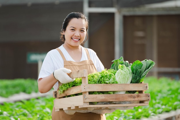 Free photo portrait of asian farmer woman holding wooden box full of fresh raw vegetables. organic farm concept.