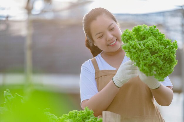 フィールドで野菜を見て、作物の品質をチェックしているアジアの農家の女性の肖像画。有機農場のコンセプト。