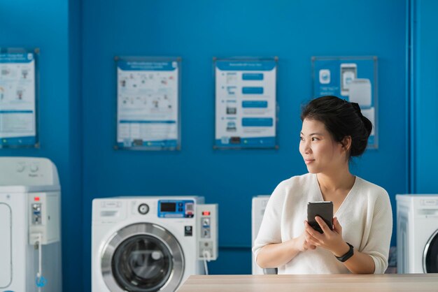 Portrait asian female hand use smartphone to check schedule of washing queue in blue color interior laundry shop in condoiminuim city lifestyle