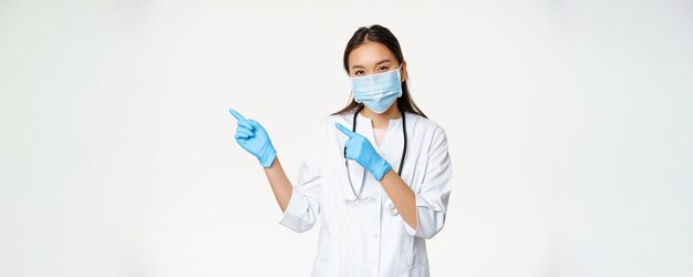 Portrait of asian female medical worker pointing fingers left wearing face mask and rubber gloves st