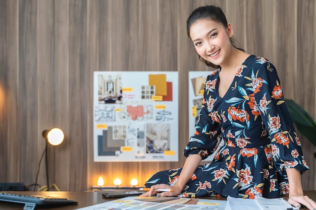 Free photo portrait of asian female woman entrepreneur smile with confident and cheerul looking at camera with background of material sample chart home office background