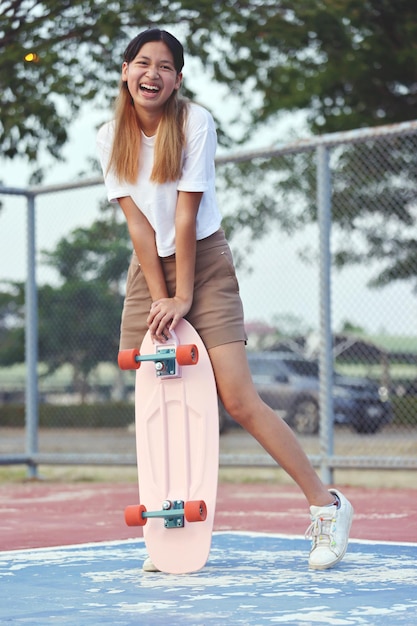 夏の日に屋外でサーフスケートを保持している肖像画アジアの女の子ティーンエイジャーのライフスタイル