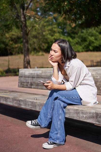 Portrait of asian girl sitting with smartphone feeling sad looking gloomy and frustrated waiting for