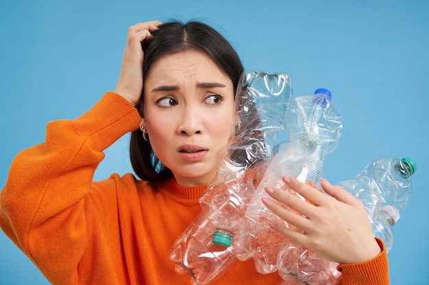 リサイクル用のペットボトルの山を持ち、怖い顔をしてこちらを見つめるアジアの女の子のポートレート