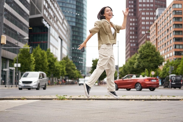 アジアの幸せな女の子の肖像画は、通りでポーズをとって市内中心部でジャンプしたり踊ったりして、喜びと元を表現します