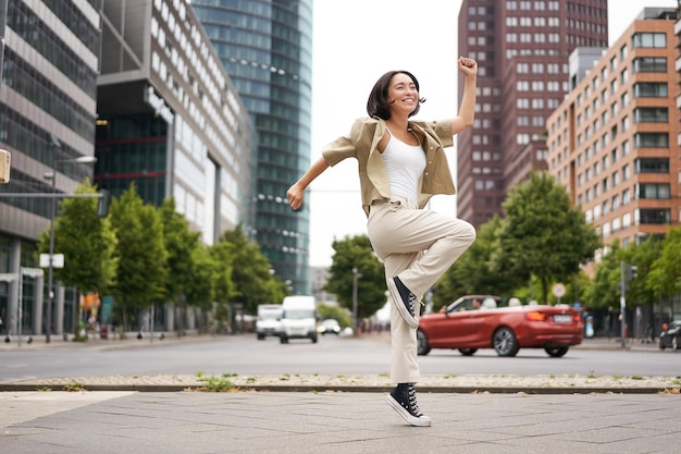 Free photo portrait of asian happy girl jumping and dancing in city centre posing on streets express joy and ex