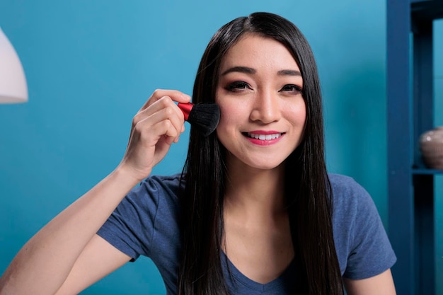 Portrait of asian influencer doing makeup tutorial in front of camera while recording content creator for vlogging channel. Vlogger woman using cosmetics brush advertising make up product