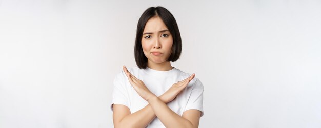 Portrait of asian korean woman showing stop prohibition gesture showing arm cross sign standing in tshirt over white background Copy space