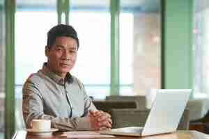 Free photo portrait of asian middle-aged businessman sitting at the office desk at laptop