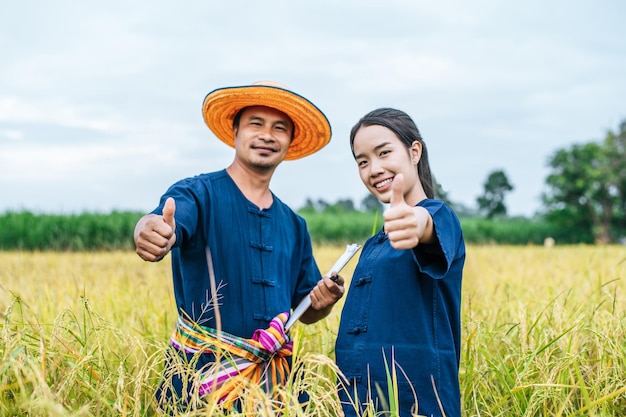 밀짚 모자와 들보를 쓴 초상화 아시아 중년 남자가 젊은 여성 농부와 함께 클립보드에 씁니다.