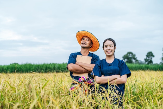 Portrait Asian Middle aged man wearing straw hat and loincloth and young woman farmer stand and cross arms in rice field together