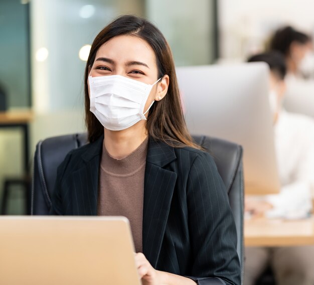 Premium Photo | Portrait of asian office employee businesswoman wear  protective face mask work in new normal office with interracial colleague  in background as social distance practice prevent coronavirus covid-19.
