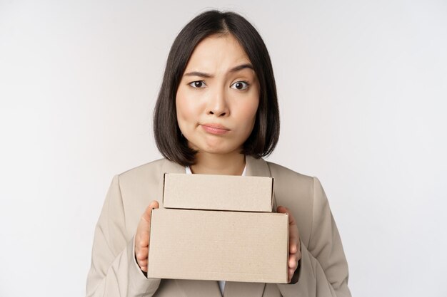 Portrait of asian saleswoman female entrepreneur holding boxes and looking sad disappointed standing over white background