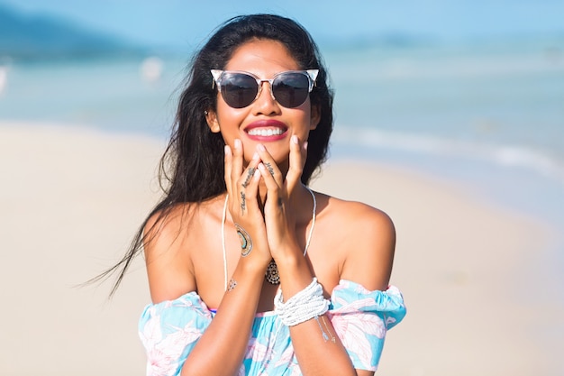 portrait of asian thai girl with sunglasses and flower dress having fun on tropical beach