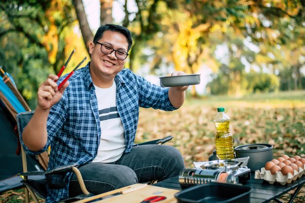 캠핑장 야외 요리 여행 캠핑 라이프 스타일 컨셉트에서 뜨거운 팬에 맛있는 계란 프라이를 튀기는 아시아 여행자 남자 안경의 초상화