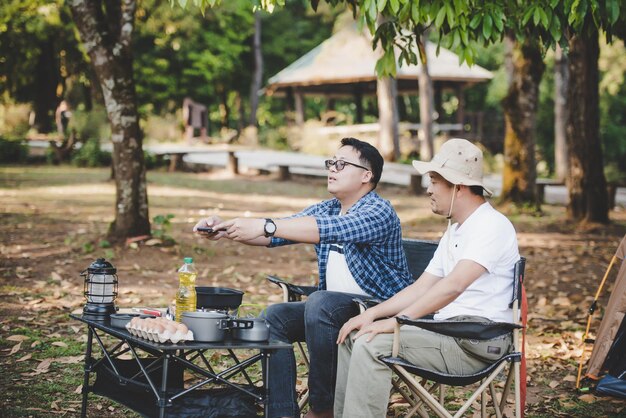 Portrait of Asian traveler men taking a photo on smartphone at a campsite Outdoor cooking traveling camping lifestyle concept