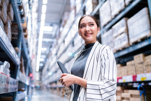 Portrait of asian woman business owner using digital tablet checking amount of stock product inventory on shelf at distribution warehouse factorylogistic business shipping and delivery service