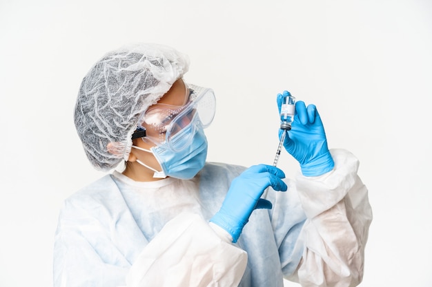 Portrait of asian woman doctor, nurse vaccinating patients, using syringe and covid-19 vaccine, standing in personal protective equipment, white background.