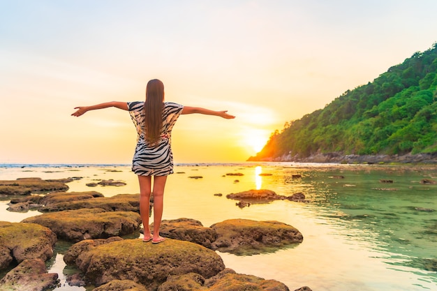 Portrait of asian woman on the rock with opened arms at sunset around ocean in vacation