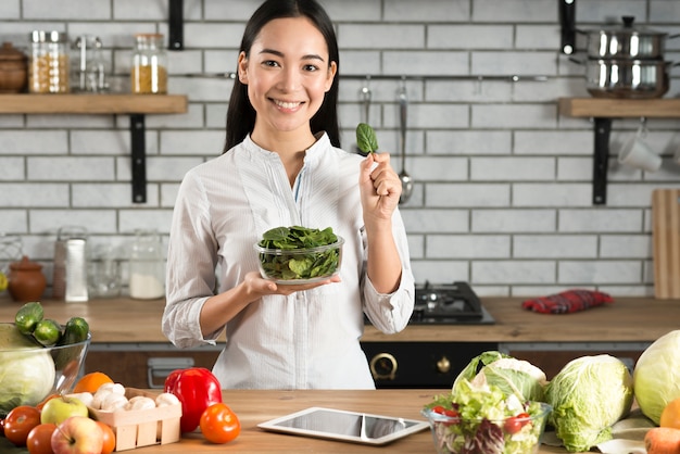 portrait of asian woman showing green basil leaves in kitchen