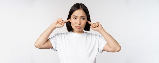 Portrait of asian woman shut ears and feeling discomfort from loud noise annoying sound standing ove...