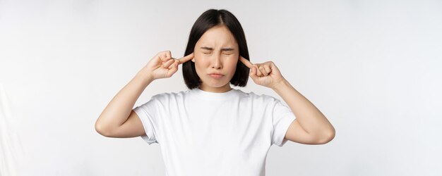 Portrait of asian woman shut ears and feeling discomfort from loud noise annoying sound standing over white background