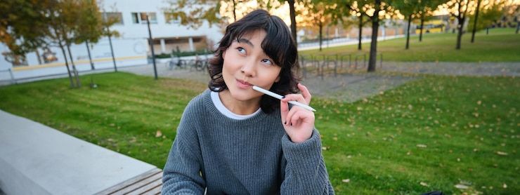 無料Photo 公園のアジア人の女性学生のポートレートは、デジタルタブレットとペンを持ってベンチに座り、考えながら探しています