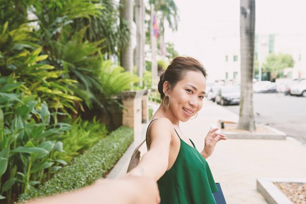 Портрет азиатской женщины, оборачиваясь и глядя на камеру, потянув руку своего неузнаваемого парня