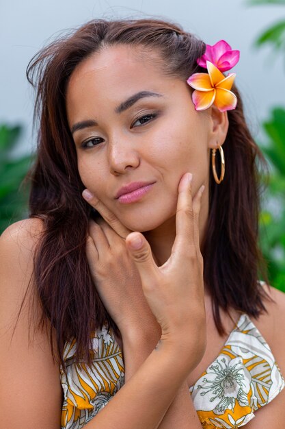 Portrait of asian woman in yellow summer dress stands with plumeria thai flower in hair and round earrings