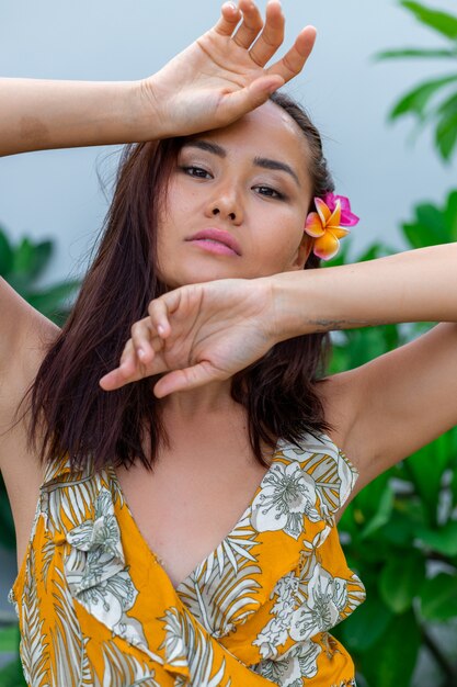 Portrait of asian woman in yellow summer dress stands with plumeria thai flower in hair and round earrings