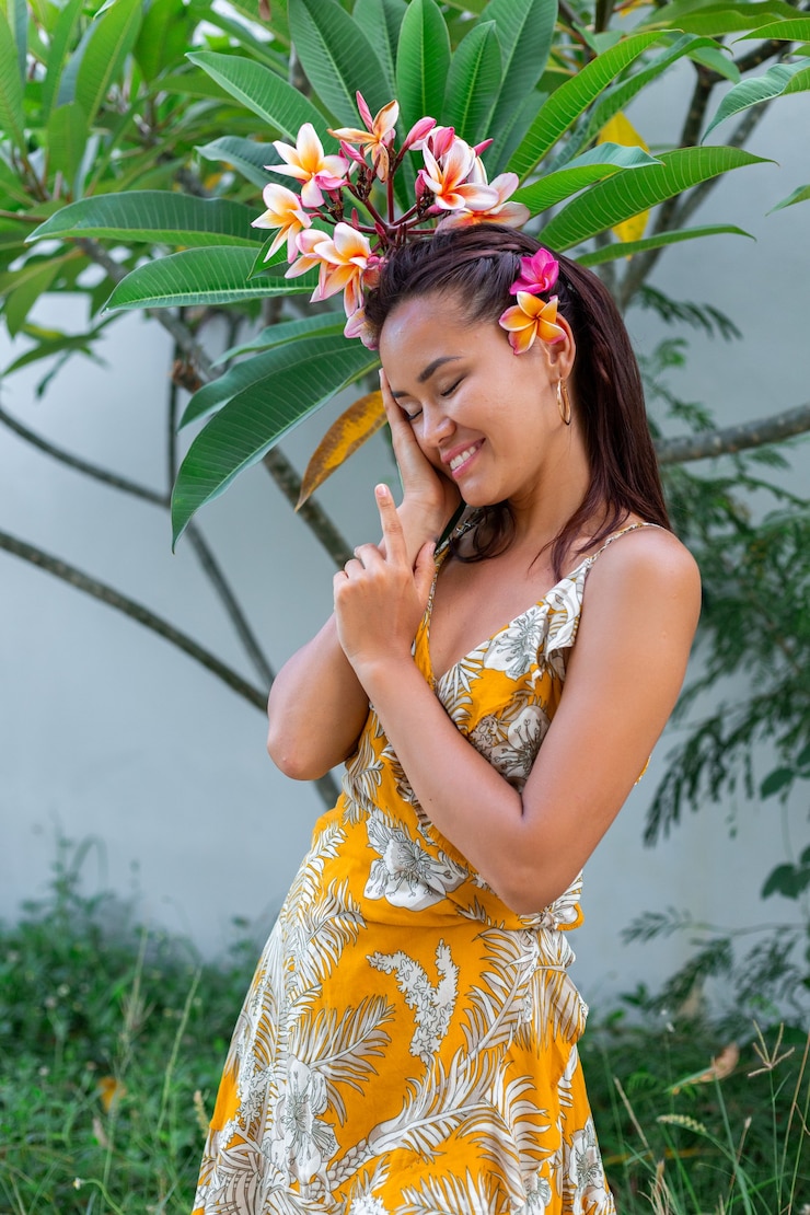 無料Photo 黄色の夏のドレスを着たアジアの女性の肖像画は、髪にプルメリアタイの花で立っています
