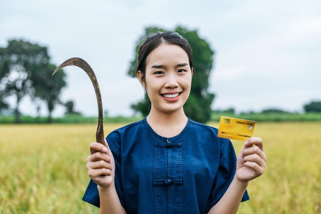 田んぼにクレジットカードを示すアジアの若い農家の女性の肖像画