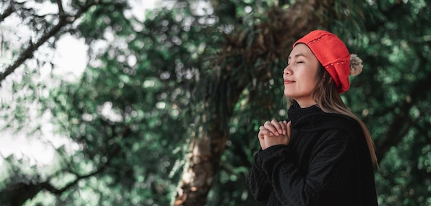 Portrait of Asian young woman in winter costume praying in the morning at the woodland Christianity and faith hope love concept