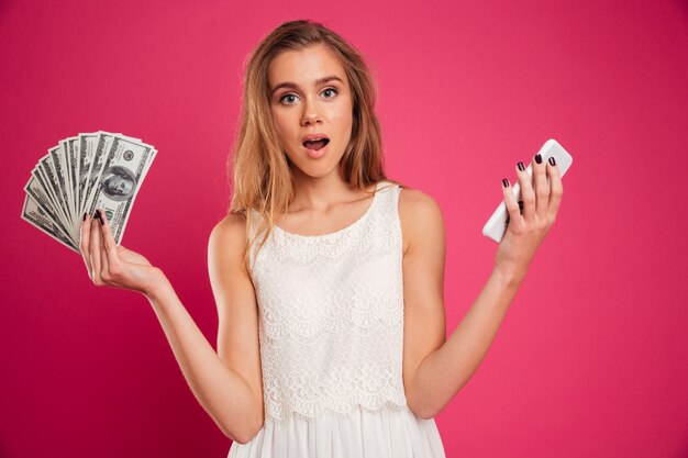 Portrait of an astonished pretty girl showing money banknotes