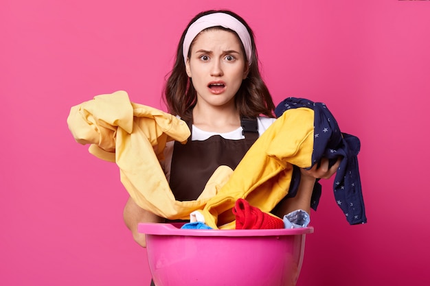 Portrait of astonished woman with huge pink basin with fresh clothes and home textile