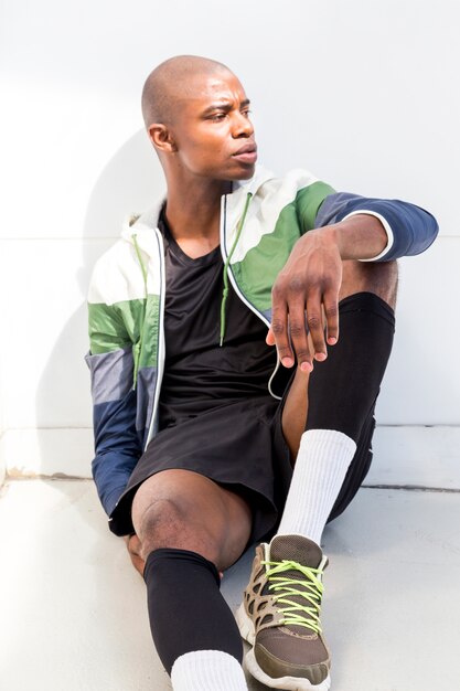 Portrait of a athlete young man sitting on floor against white wall