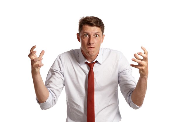 Portrait of an athletic brunet person with brown eyes, wearing in a white shirt and a red tie. He is looking very angry while posing in a studio isolated over a white background. Concept of gesticulat